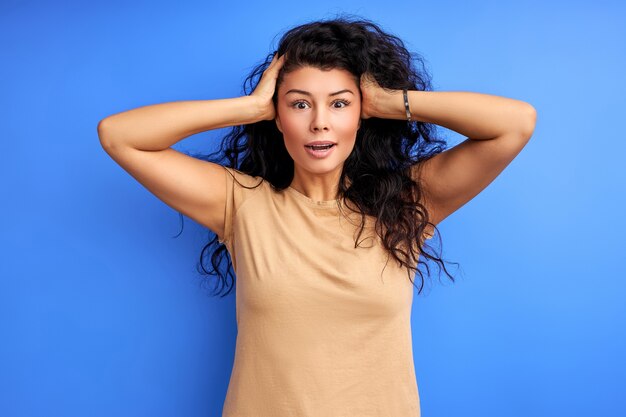 Woman remembered something, holding hands on head, stand in shock. isolated blue wall