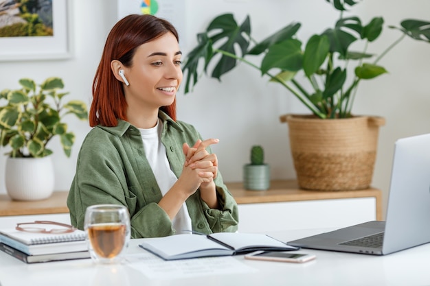 Woman remotely working at home with laptop Young businesswoman talking via wireless earphones