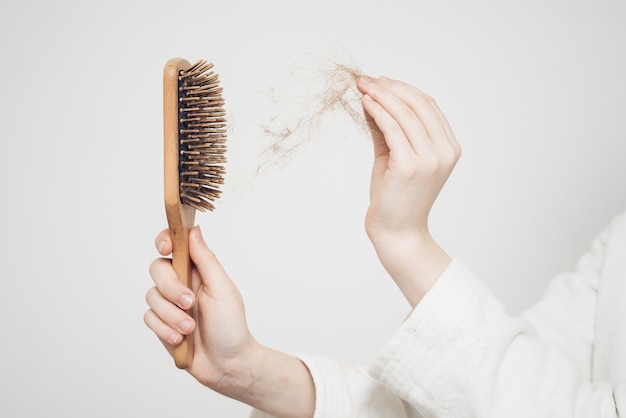 Woman removes a bun of hair with a wooden comb on a light wall\
health problems loss.