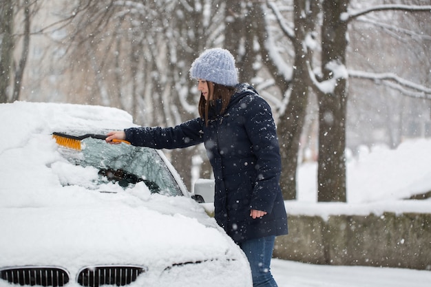 Женщина, удаляющая снег с лобового стекла автомобиля