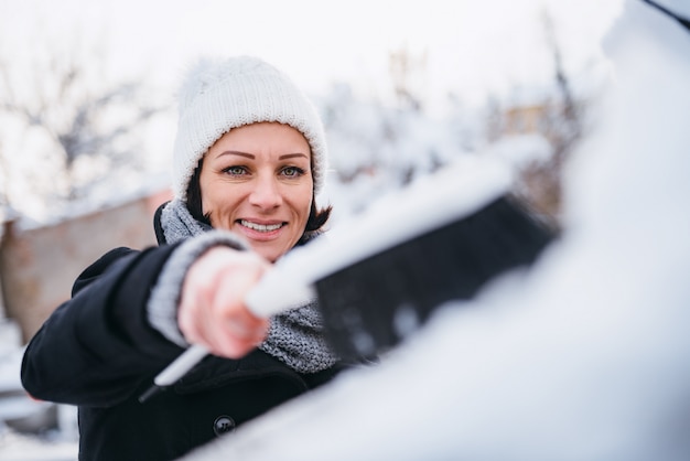 Foto donna che rimuove neve dall'automobile