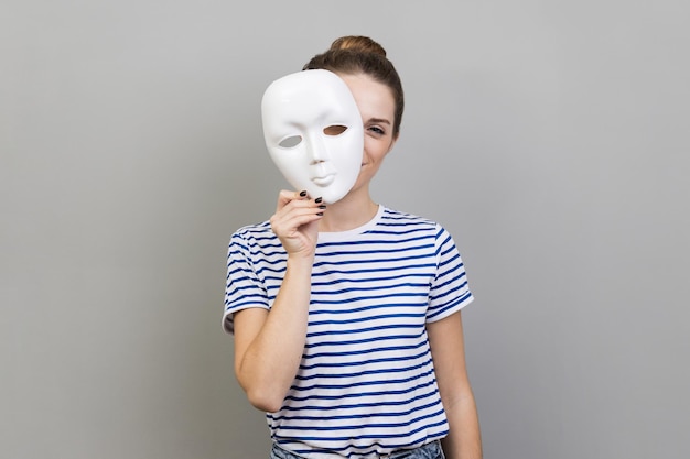 Woman removing white mask from face showing his smiling expression pretending to be another person