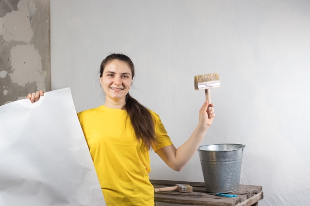 A woman repairman glues white wallpaper on the wall.