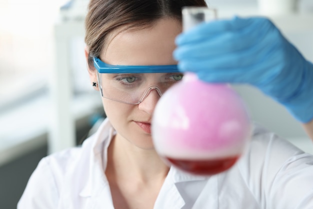 Женщина-исследователь в очках проводит химический эксперимент в колбе