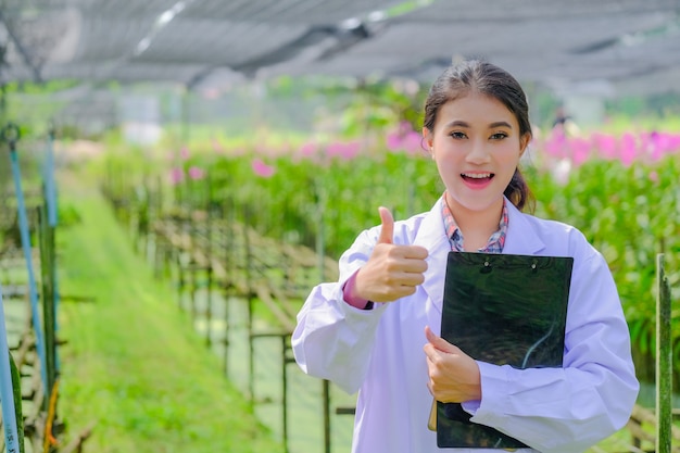 Woman researcher in a white dress, thumbs up and explores the garden 