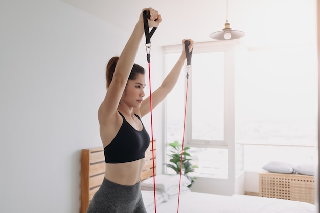 La donna fa l'allenamento con la fascia di resistenza sulla parte superiore del torace nella sua camera da letto