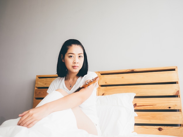 Woman rest on her bedroom with ukulele.