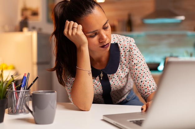 Woman resting eyes while working from home kitchen during a deadline late at night