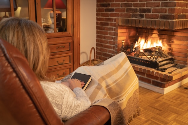 Woman resting in front of the fire in a fireplace in an armchair and covered with a blanket.