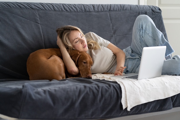 Woman resting lying on couch working on laptop with lovely Vizsla dog at home top view. Lazy pastime