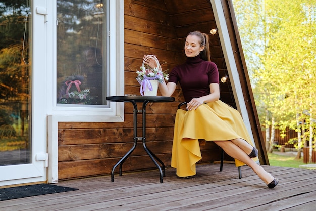 小さな家のテラスで休んでいる女性がバスケットの中の花を見ています