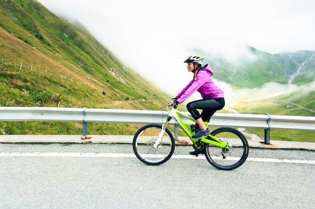 Woman riding bicycle on road against cloudy sky
