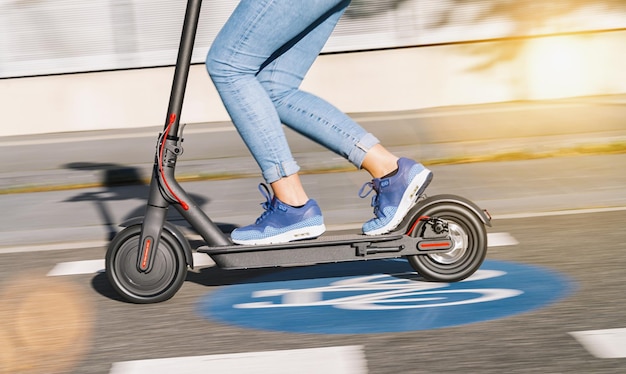 женщина едет на электрическом самокате или электронном скутере над дорожным знаком "Велосипед" на городском пейзаже, размытие движения