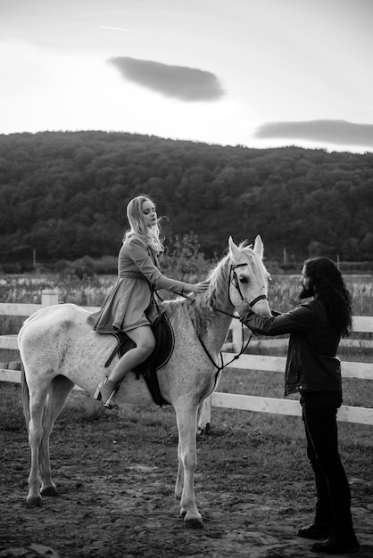 Woman riding grey arabian horse in pink dress handsome bearded man driving horse for a bridle and lo