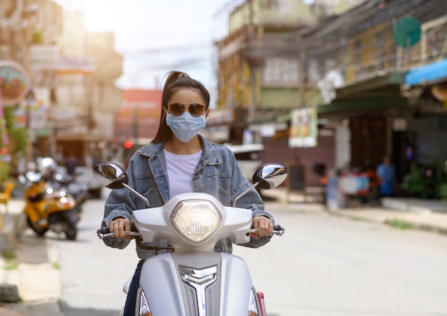 Donna in sella a una moto che indossa una maschera in città