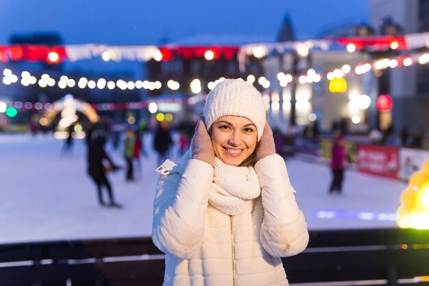 A woman on the rink is skating and taking selfie on smartphone. New Years Eve and Christmas. Fairy lights. Ice and snow mood concept. Winter