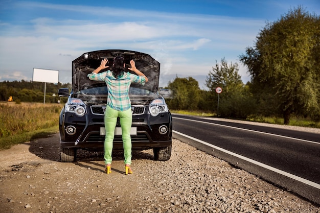 Woman on the road near the car. Damage to vehicle problems on the road.