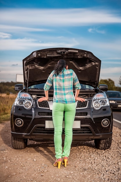 Woman on the road near the car. Damage to vehicle problems on the road.