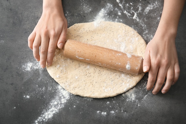 Woman rolling dough with poppy seeds on table, closeup