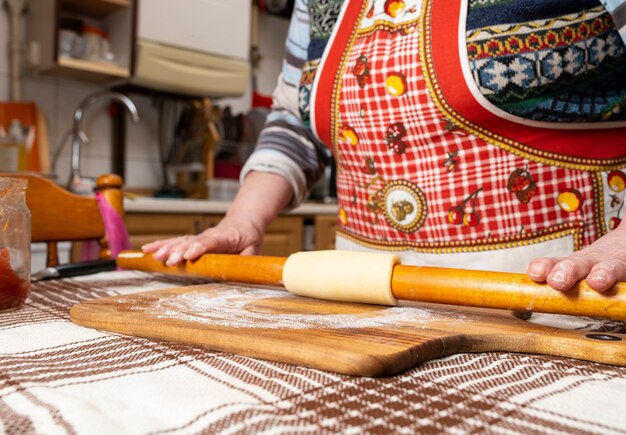 台所のテーブルにめん棒で生地を伸ばす女性。生地、ピザ、ベーキングの調理の概念