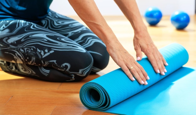 Woman rolling a yoga mat on wooden floor