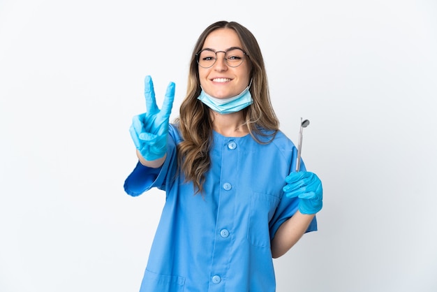 Woman Romanian dentist holding tools over on pink smiling and showing victory sign