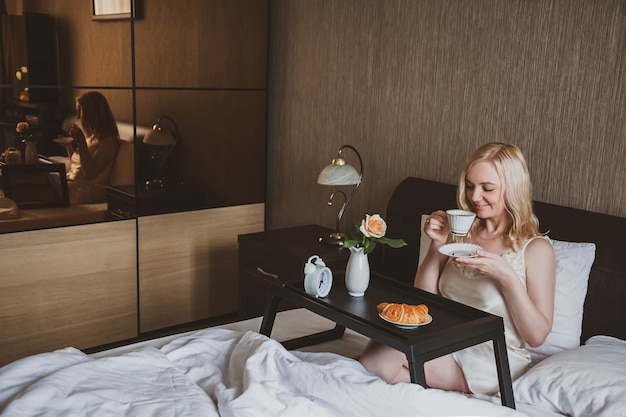 A woman in room drinks coffee sitting in bed