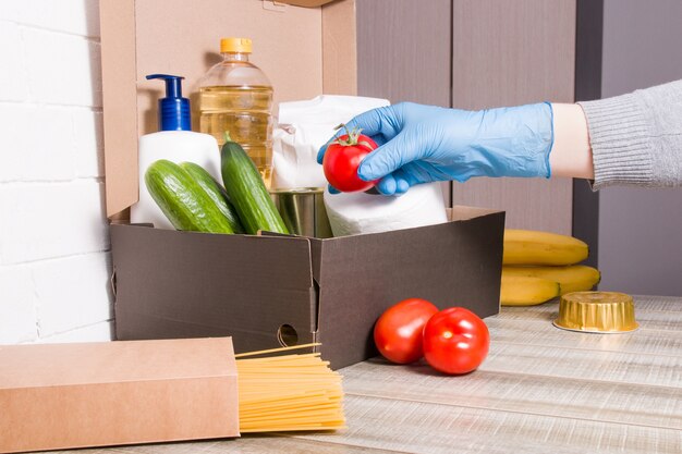 A woman in a rubber glove sweetens a red tomato in a box with products for donation