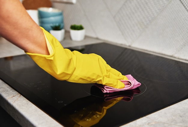 Женщина в резиновых перчатках чистит индукционную плиту