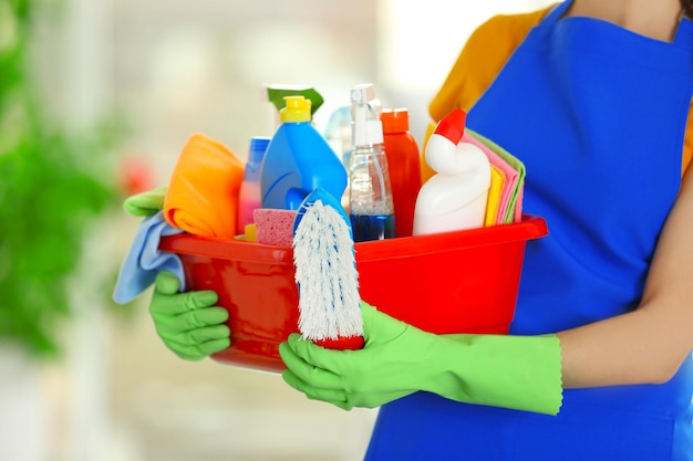 Photo woman in rubber gloves holding basin with detergents on blurred background