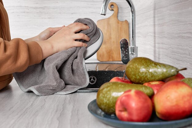 A woman rubs a dish with a terry towel in the kitchen