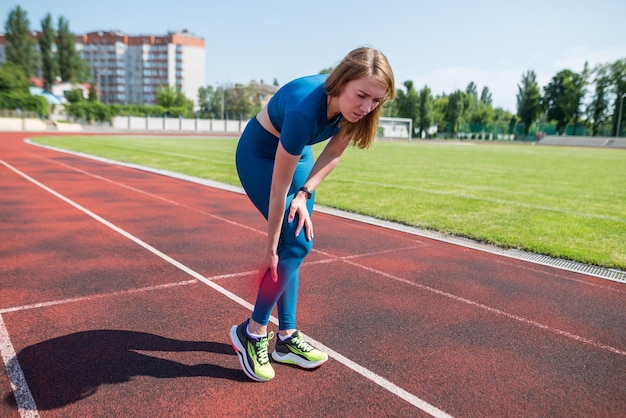 トレッドミルでスポーツの脚を負傷した女性ランナーを抱え、屋外で走った後、脚の痛みに苦しんでいる女性ランナー