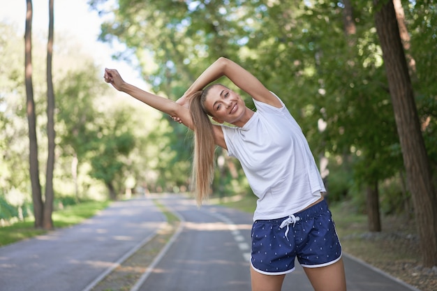 サマーパークの朝を運動する前に腕を伸ばす女性ランナー