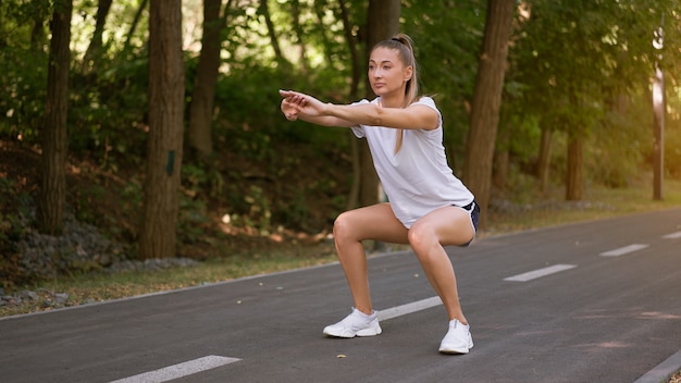 Woman runner stretching legs before exercising summer park\
morning