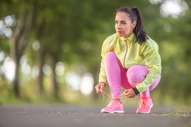 Woman runner tying shoelaces before jogging in autumn tree alley park.