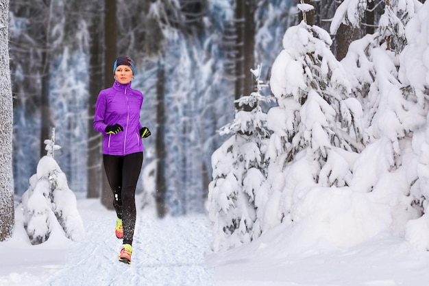 写真 森の雪に覆われた歩道で走っている女性