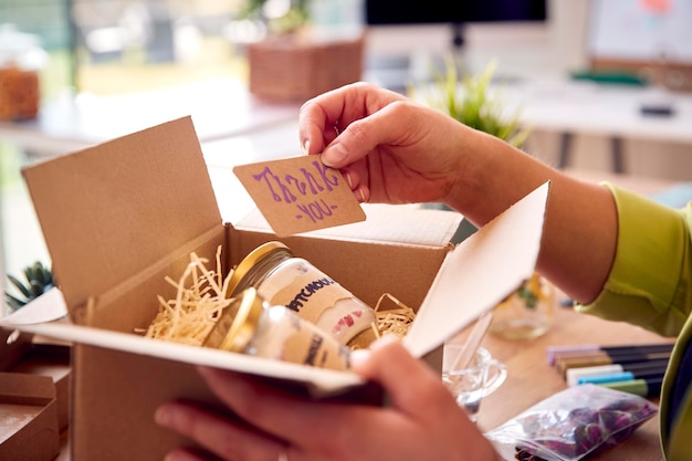Женщина, занимающаяся онлайн-бизнесом из дома, упаковывает и маркирует бутик-свечи, готовые к отправке