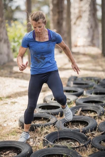 Donna che corre sopra il pneumatico durante il percorso ad ostacoli nel campo di addestramento