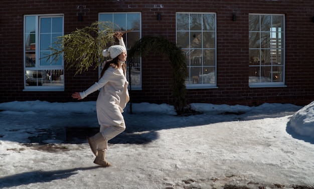 Женщина бежит с елкой на заднем дворе дома зимой