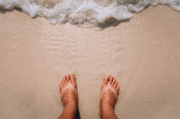 Woman's feet are standing near the sea waves on the pink beach