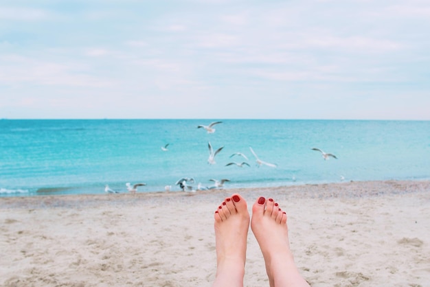 Photo woman's feet with red nails on the sea shore background