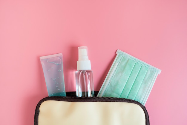 Foto borsa a mano da donna con mascherina chirurgica, gel per mani alcolico. articoli igienici medici su sfondo rosa con spazio di copia. protezione covid-19, diffusione del coronavirus. concetto di sanità vista dall'alto, piatto laico