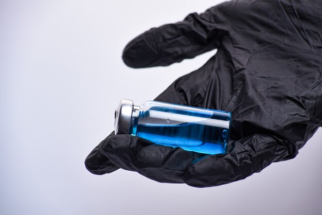 A woman's hand in black gloves holds an ampoule.