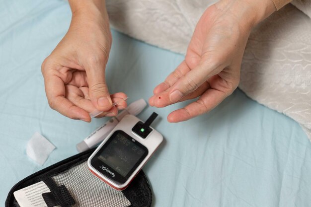 Photo a woman's hand checking her blood sugar level with a glucometer by herself at her home