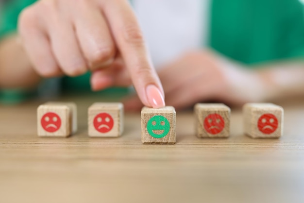 Woman's hand chooses happy emoji from wooden cubes with sad and happy emoji