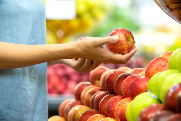 Woman's hand choosing red apple in supermarket.