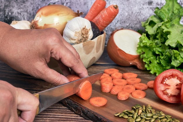 Woman's hand cutting carrot and other vegetables to make a salad on vintage wooden background. Healthy vegetarian food.