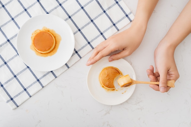 La mano della donna che taglia il budino fatto in casa della crema al caramello sul piatto bianco