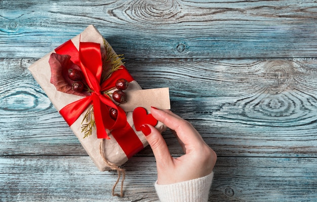 A woman's hand decorates the heart of a gift box on a wooden background.