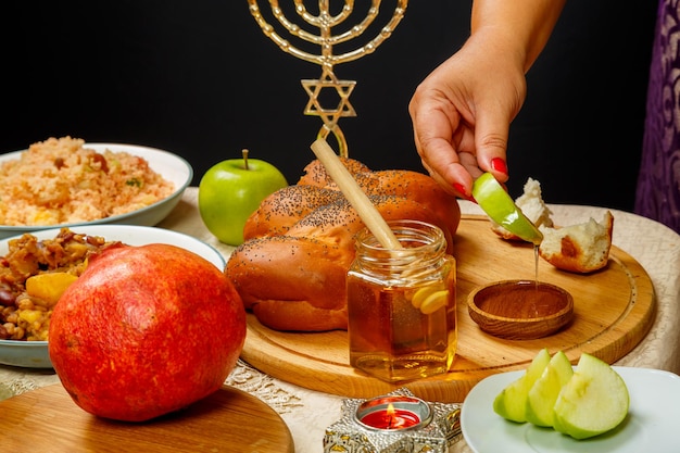 A woman's hand dips an apple in honey at a meal at the festive table in honor of Rosh Hashanah